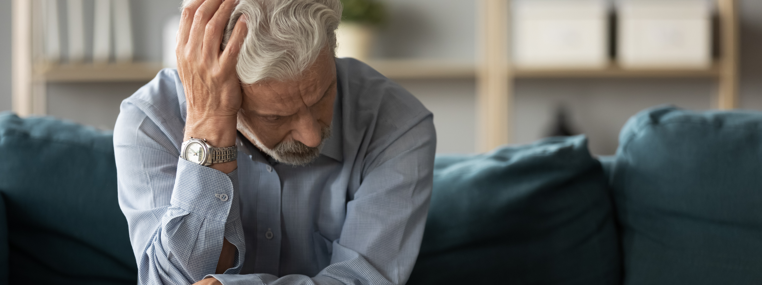Mann sitzt auf dem Sofa und greift sich an den Kopf.